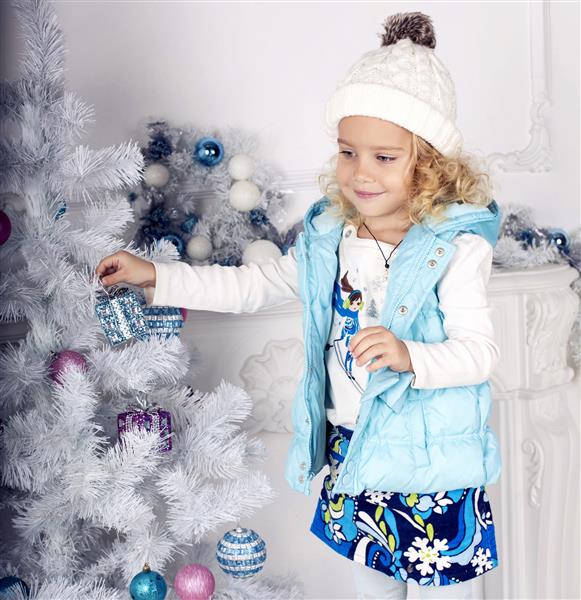 عکس زیبا از دختر بچه ناز 5 ساله با موهای فر مو بور و تزئین درخت کریسمس در خانه