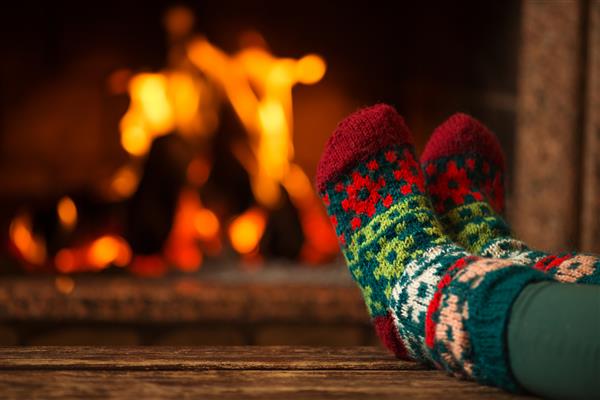پا در جوراب های پشمی کنار شومینه قرار دهید زن با آتش گرم و گرم شدن پاهایش در جوراب های پشمی آرام می شود نزدیک روی پا مفهوم تعطیلات زمستانی و کریسمس