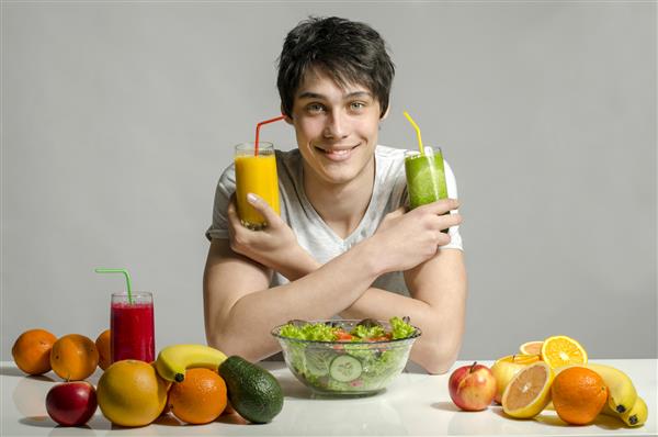 مردی که میز پر از غذای ارگانیک آب میوه و اسموتی دارد یک جوان خوش روح که سالاد و میوه های سالم می خورد جدا شده روی سفید
