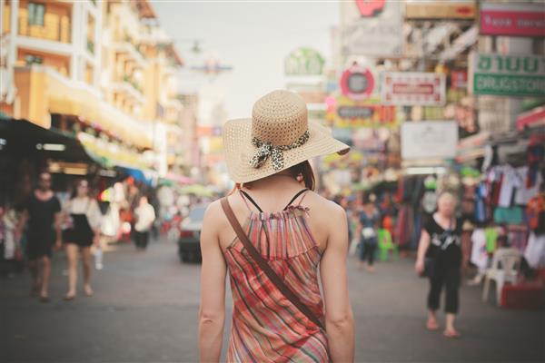 نمای عقب زن جوانی که در خیابان معروف کوله پشتی در بانکوک تایلند قدم می زند