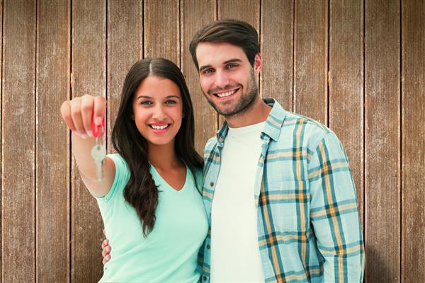 زن و شوهر جوان شاد نشان دادن کلید خانه جدید در برابر تخته های چوبی