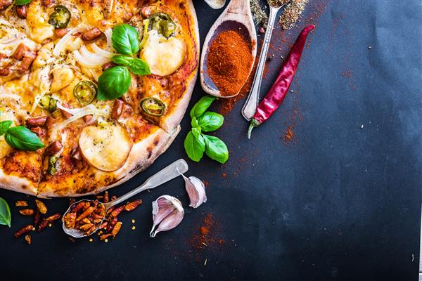 پیتزای خوشمزه روی زمینه سیاه همراه با ادویه جات و سبزیجات