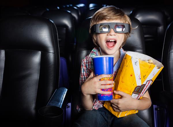 پسری متعجب که در حین تماشای فیلم سه بعدی در تئاتر سینما تنقلاتی در دست دارد