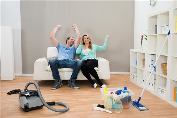 زن و شوهر خوشحال که روی مبل با لوازم تمیز کردن در طبقه بلند می شوند