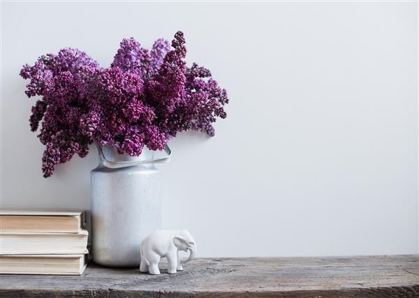 دکوراسیون داخلی منزل دسته گل یاس بنفش در گلدان و کتابهایی روی میز چوبی روستیک روی زمینه دیوار سفید