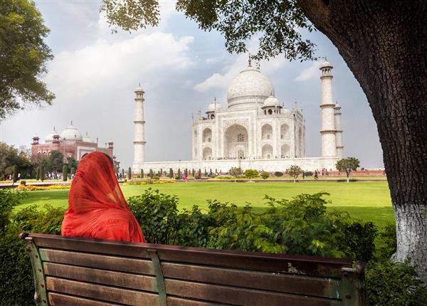 زنی با روسری قرمز روی نیمکت در سایه نشسته و به تاج محل در آگرا اوتار پرادش هند نگاه می کند