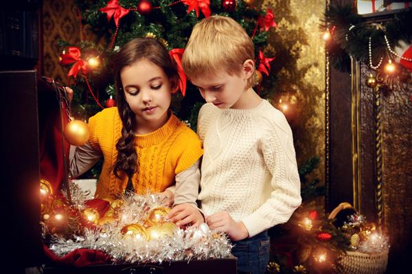 دو کودک با هدیه کنار درخت کریسمس در خانه