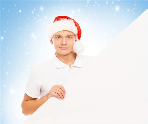 یک جوان خوش تیپ با یک تابلوی تبلیغاتی خالی و کلاه کریسمس در پس زمینه زمستان