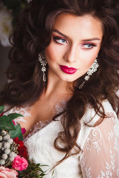 نمای نزدیک از عروس زیبا با لباس سفید با آرایش موی زیبا و آرایش دسته گل در دست