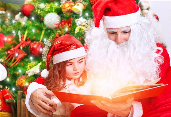 دختر کوچک ناز و بابا نوئل که کنار درخت کریسمس نشسته