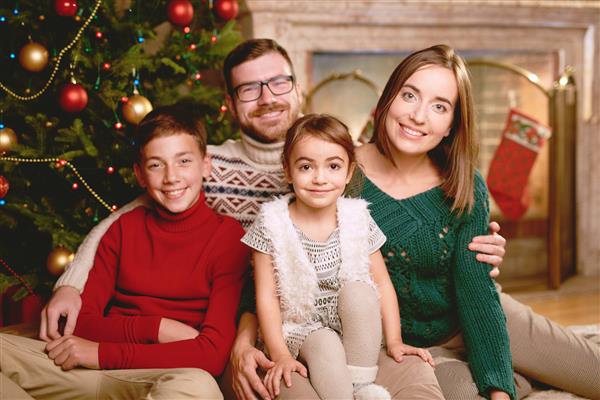 خانواده چهار نفری شادی که عصر کریسمس به دوربین نگاه می کنند