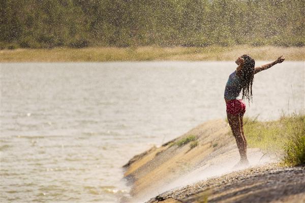 زن زیبا از باران در روز آفتابی نزدیک به یک دریاچه لذت می برد