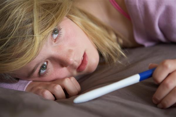 دختر نوجوان افسرده با تست بارداری در اتاق خواب نشسته است