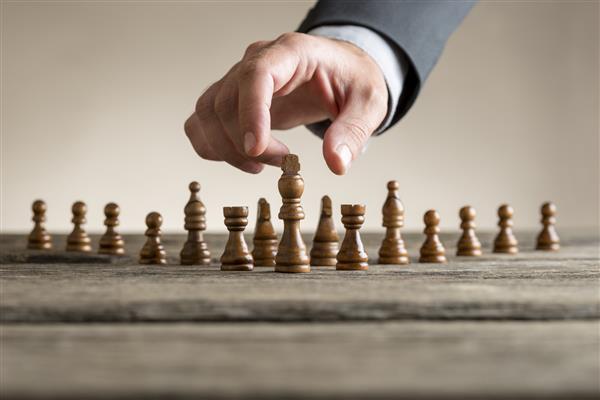 دست انسان کت و شلوار پوشیده و مهره شطرنج شاه پشت میز مفهومی پیشرفت و موفقیت