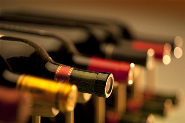 بطری های شراب قرمز روی قفسه های چوبی انباشته شده با عمق میدان محدود