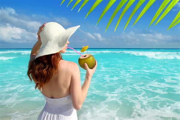 مدل زن در حال نوشیدن کوکتل نارگیل در کنار ساحل