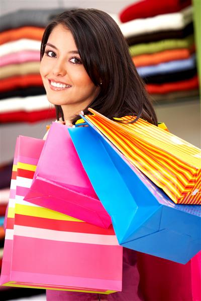 دختری در یک فروشگاه لبخند می زند و کیف های خرید به همراه دارد