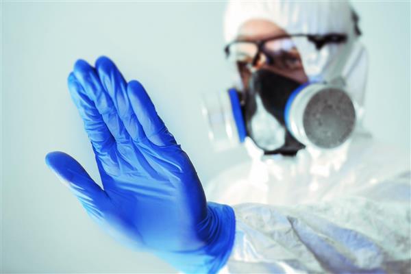 پرستاری که ماسک زده است با دستکش آبی خواستار جلوگیری از ویروس کرونا است