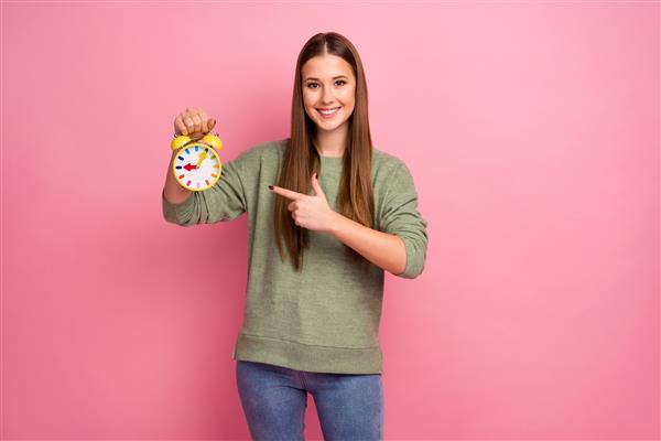 دختر شاد مثبت ساعت را با انگشت اشاره نشان می دهد زمان را نشان می دهد
