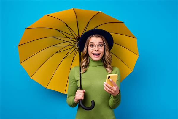 دختری با کلاه و عینک که چتر و تلفن را در دست دارد