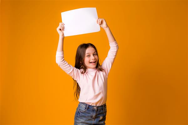 دختر بچه لبخند می زند و یک ورق خالی را در زمینه زرد در دست دارد