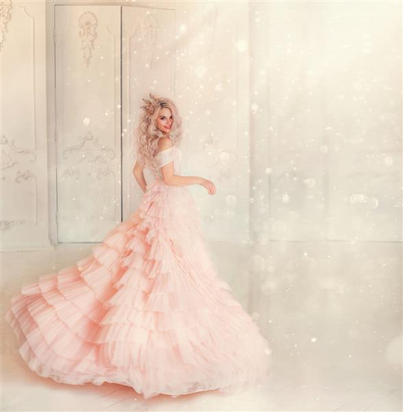 مدل زن جوان شاد در حال رقصیدن با لباس صورتی در اتاق سلطنتی سفید موهای بلوند ملکه تاج طلایی ماژیک نور درخشان می درخشد ژست دعوت تعطیلات کارناوال فضای خالی پس زمینه