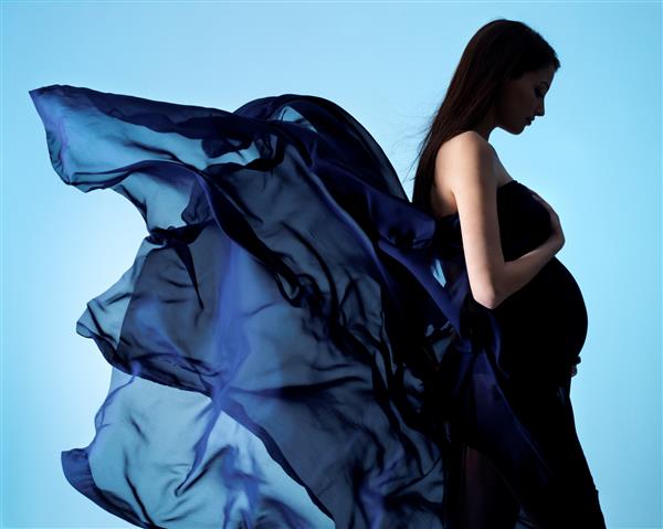 زیبایی و زرق و برق زن باردار جوان با لباس ابریشمی آبی روی آبی
