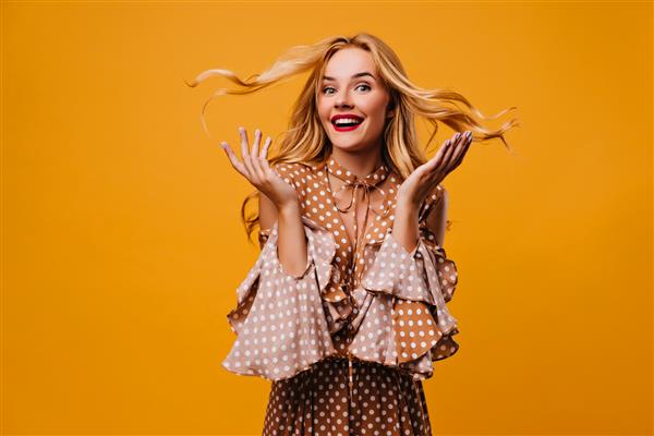 مدل زن Debonair در بلوز کلاسیک ابراز شگفتی عکس داخل خانه از دختر مثبت که با لبخند متعجب روی دیوار زرد ژست گرفته است