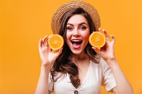 زن جذاب با چشمان سبز با لذت به دوربین نگاه می کند و پرتقال ها را در پس زمینه ای جدا نگه می دارد