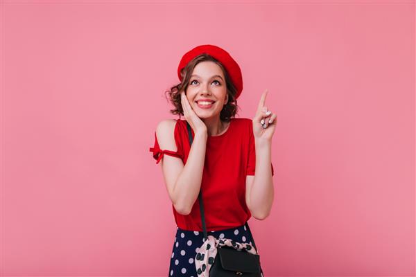 دختر فرانسوی شگفت انگیز با مدل موی موج دار که با لبخند متعجب ژست گرفته است عکس داخلی از زن سفید برازنده با کلاه قرمز جدا شده