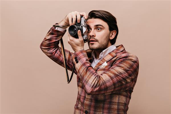 عکاس جوان مضطرب با موهای تیره با کت شطرنجی دوربین را در دست گرفته و به کناری نگاه می کند
