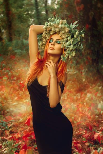 بانوی لاغر جنسی با تاج گل رازک روی سر در جنگل در حال ژست گرفتن در فضای باز