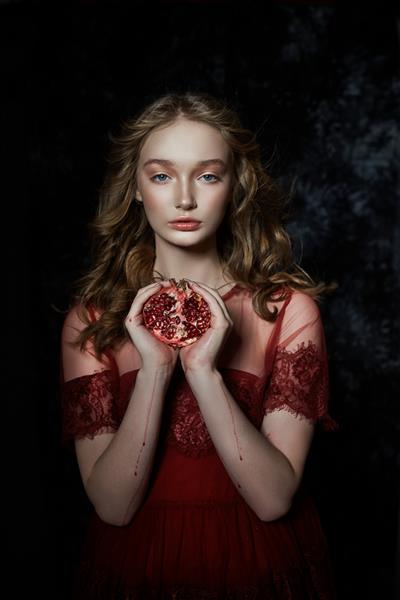 دختر بلوند زیبا با میوه انار در دستانش پرتره بهاری دختری با لباس قرمز در حال شکستن انار آب در دستانش جاری است