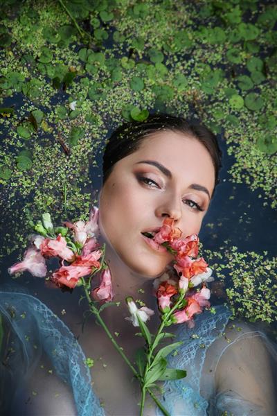 زن زیبای عاشقانه هنری با لباس بلند آبی با گل در باتلاق خوابیده است پرتره سبزه با لباس شفاف در باتلاق آب گل اردک جلد کتاب