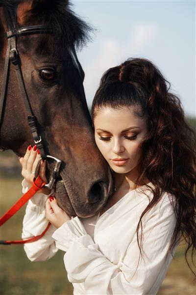 زن زیبا اسبی را نوازش می کند و افسار را در مزرعه می گیرد
