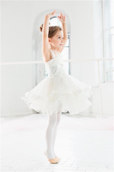 دختر بالرین کوچولوی توتو کودک شایان ستایش در حال رقص باله کلاسیک در یک استودیو سفید