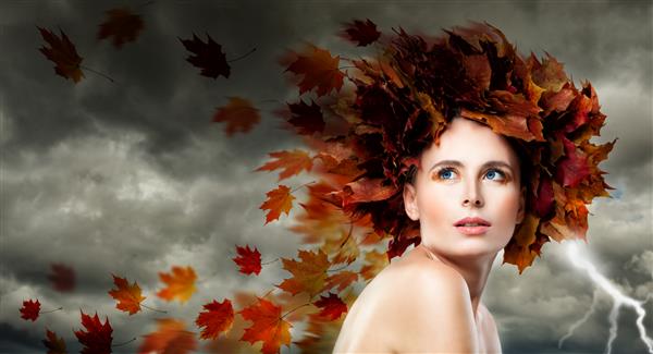 زن مدل زیبا با برگ های پاییزی آسمان ابری طوفانی دمیدن برگ ها آرایش مد و زیبایی کامل