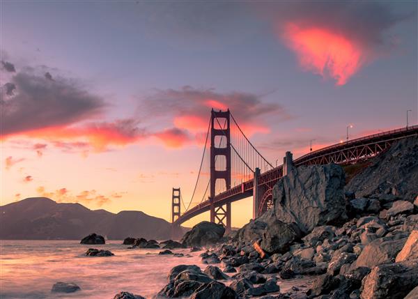 پل دروازه طلایی روی بدنه آب در نزدیکی سازندهای سنگی در هنگام غروب خورشید در سان فرانسیسکو کالیفرنیا