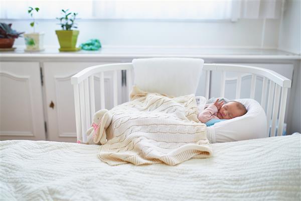 نوزاد دختری که در گهواره همخوابی که به تخت والدینش چسبیده است چرت می زند