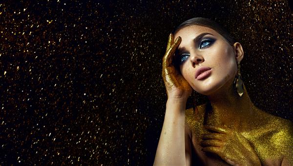 صورت و دستان یک دختر جوان زیبا و خودنمایی با آرایش روشن و موهای شانه شده در برق های طلایی براق روی پس زمینه مشکی