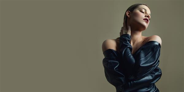 دختر جوان زیبا با رژ لب روشن در لباس چرمی مشکی که در استودیو ژست گرفته است تاکید بر دست ها