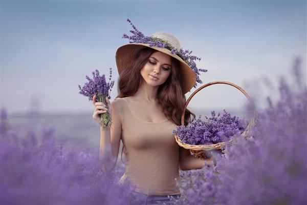 پرتره زن زیبا در مزرعه اسطوخودوس در پروونس دختری جذاب با موهای مجعد بلند با کلاه حصیری که گل های بنفشه در دست دارد سبزه بی دغدغه که از زندگی لذت می برد و در غروب آفتاب رویا می بیند