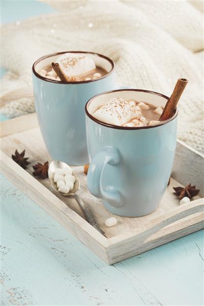 فنجان های آبی نوشیدنی شکلات داغ با مارشمالو و دارچین در زمینه چوبی آبی زمان زمستان مفهوم تعطیلات تمرکز انتخابی تون