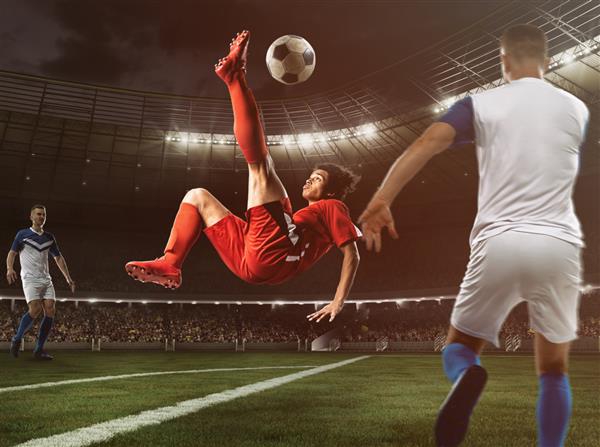 مهاجم فوتبال با لباس قرمز با یک ضربه آکروباتیک در هوا در ورزشگاه به توپ ضربه می زند