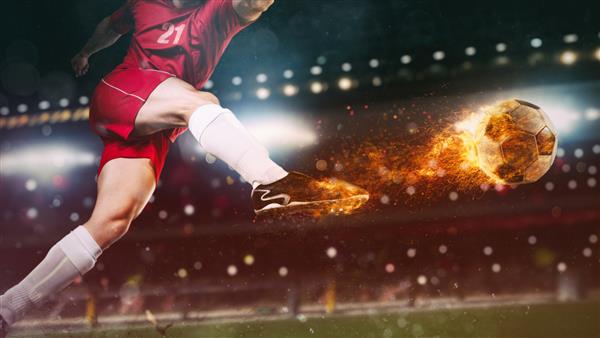 نمای نزدیک از یک صحنه فوتبال در مسابقه شبانه با بازیکنی با لباس قرمز در حال لگد زدن به توپ آتشین با قدرت