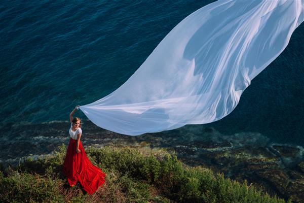 دختر زیبا با لباس قرمز با پارچه سفید در زمینه دریا