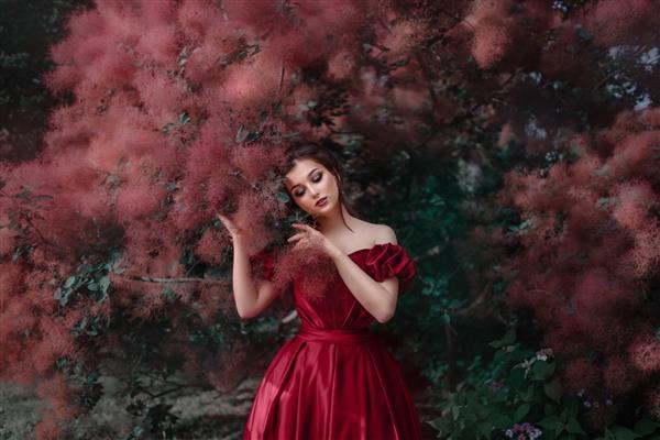 زن زیبا با لباس قرمز در حال قدم زدن در باغ پر از گل رز