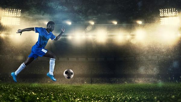 بازیکن فوتبال با لباس آبی که به سرعت با توپ در استادیوم می دود