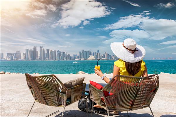 زنی با آبمیوه در دست از منظره افق دوحه قطر در یک روز آفتابی لذت می برد