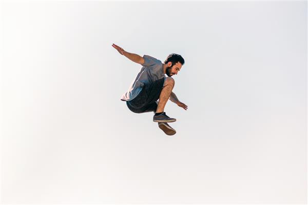 مرد ورزشکار در حال تمرین پارکور هنگام پریدن در هوا